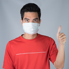 Sick young man wearing medical mask and red shirt thumbs up sign isolated on gray wall background. Concept of headache. Asia people.