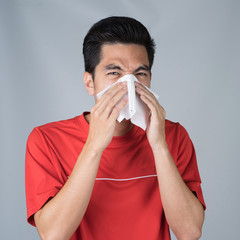 Sick young man handsome and sneeze wearing medical mask and red shirt isolated on gray wall...