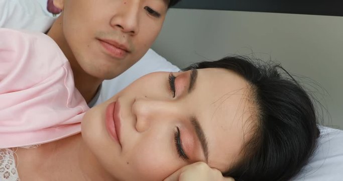 Close up scene video of good ooking Asian couple lying on bed, man kissing on woman's cheek, concept for happy lover in bedroom.