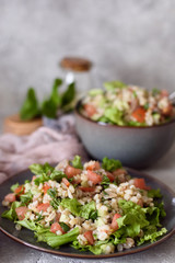 Taboule with pearl barley porridge with fresh vegetables and herbs on a plate and bowl on a gray concrete background