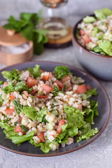Taboule with barley porridge with fresh vegetables and herbs on a gray concrete background
