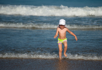 Small happy girl in swimsuit plaing with waves on the sea shore