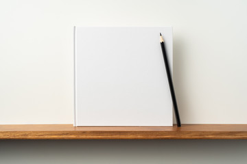 white square notebook on bookshelf and white wall