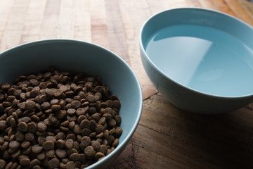 Obraz na płótnie Canvas cat food dishes - close up of two blue bowls of cat dry food and water standing on a wooden table
