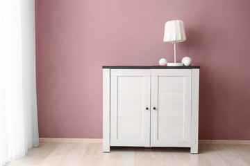 Stylish commode with lamp near color wall in room