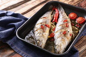Baking tray with tasty cooked fish on wooden table