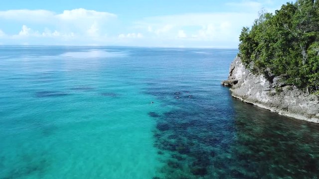 People are swimming in the ocean near a cliff with trees on the Togean Island near Sulawesi in Indonesia