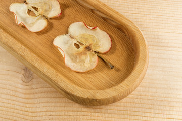 Close-up part of oblong wooden plate with apple chips on  wooden background.