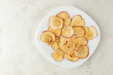 White square plate with apple chips on textured white background.