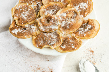 Close-up apple chips sprinkled with powdered sugar and cinnamon on white plate on kitchen towel.
