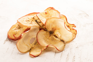 Heap of dried apple chips on white textured background.