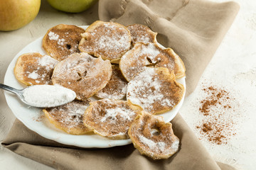 Apple chips sprinkled with powdered sugar and cinnamon and spoon on plate on beige fabric.