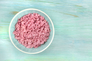 A bowl of pink Himalayan sea salt, shot from above on a teal blue background with copy space