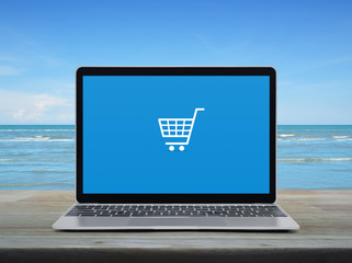 Shopping cart flat icon with modern laptop computer on wooden table over tropical sea and blue sky...