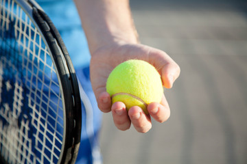 Sportsman is playing tennis on court outdoor. Male hand holds tennis racket and gives yellow ball. Man has workout. Sports activities in summer.