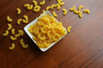 White bowl with dried pasta on a wooden table, top view. Photo with blank space for text.