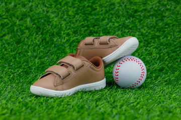 Concept encourage children to play sport, exercise for a healthy body, shoes of small baby shoes next to ball isolated on grass background.