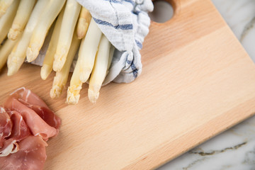 Roher, weißer Spargel in Tuch mit geräucherten Schinken auf Holz Brett und Marmor Hintergrund