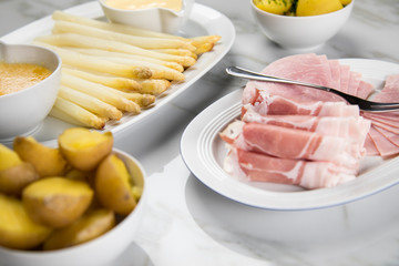 Platte weißer Spargel mit Sauce Hollandaise, zerlassener Butter, Kochschinken, geräucherten Schinken und Kartoffeln auf Marmor Hintergrund