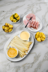 Platte weißer Spargel mit Sauce Hollandaise, zerlassener Butter, Kochschinken, geräucherten Schinken und Kartoffeln auf Marmor Hintergrund