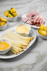 Platte weißer Spargel mit Sauce Hollandaise, zerlassener Butter, Kochschinken, geräucherten Schinken und Kartoffeln auf Marmor Hintergrund