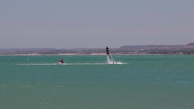 shot over the ocean of a person riding a flyboard behind a jet ski.