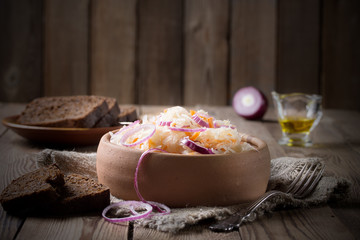 Sauerkraut with rings of onions, in a pottery with black bread, on a wooden table.