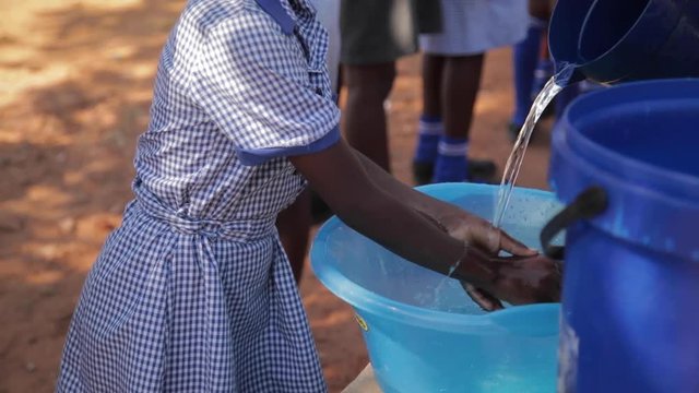 African school pupils wash their hands outside in a plastic dish with water poured from a jug before mealtime