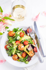 Delicious fresh salad with prawns, greens, cucumber, avocado and tomato. with white wine and flowers on light background