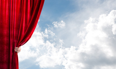 Cloudy landscape behind red curtain and hand holding it