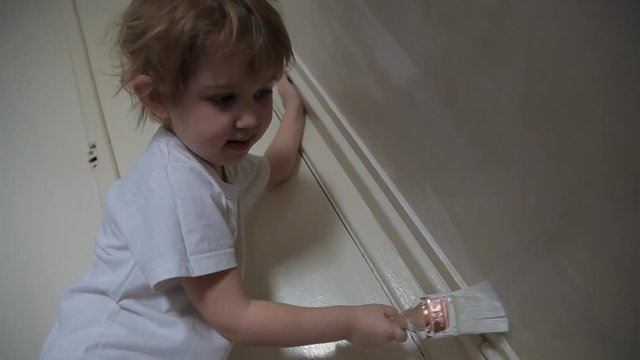 little cute girl paints the wall with paint and brush and smiles
