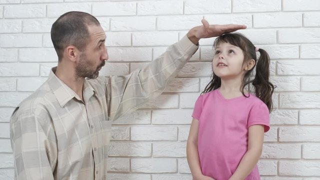 Measure the child's height. Father shows daughter how she grew up.