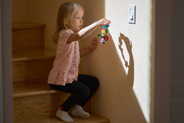 Little girl is sitting on the floor, playing lonely. On the wall is a diffractive from hand shadow...