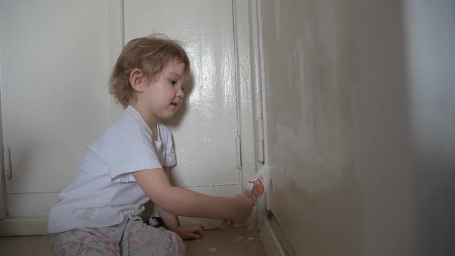 a little cute cheerful girl paints the door with a brush and paint and makes a surprised face