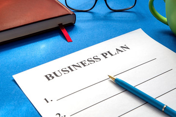 A business plan template to fill out with pen, coffee, glasses and on blue table.