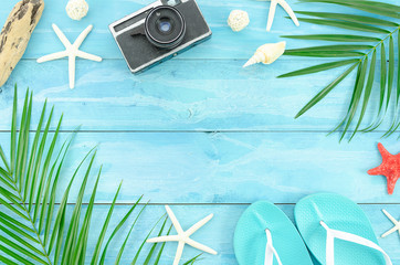 Fototapeta na wymiar Top view traveler accessories, tropical palm leaf branches on wooden planks background with empty space for text. Travel vacation concept. Summer background with starfishes, and beach slippers