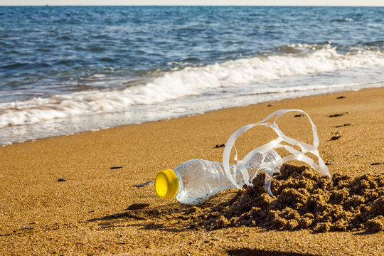 Plastic Pollution. A Plastic Bottle And A Six Pack Plastic Rings On The Beach Shore