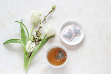 Spring blossoms and a cup of tea with a heart shape tea bags on a bright background, flat lay style with a copy space