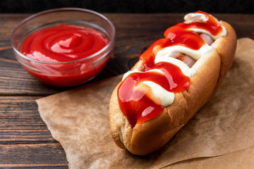 Hot dog with mayonnaise and ketchup on dark wooden background.