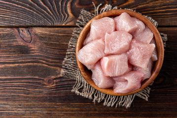 Diced raw chicken breast or fillets on dark wooden background. © Natallia