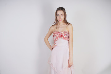 a charming young caucasian girl stands in a pink long prom dress with flower petals on her chest and poses on a white background in the Studio