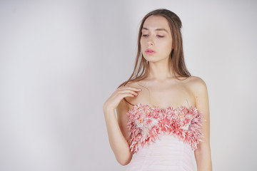 a charming young caucasian girl stands in a pink long prom dress with flower petals on her chest and poses on a white background in the Studio