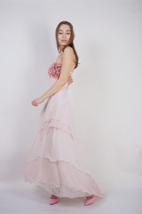 Fototapeta na wymiar a charming young caucasian girl stands in a pink long prom dress with flower petals on her chest and poses on a white background in the Studio