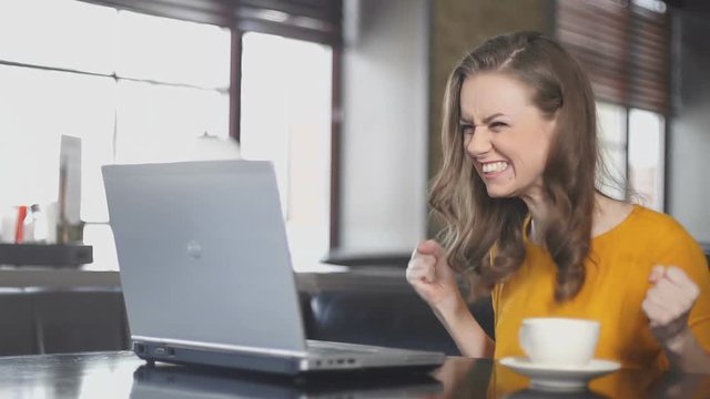 Excited woman using laptop in cafe, winning online lottery, dance of victory