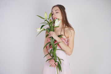 charming young caucasian girl in a pretty dress holds a lush Lily flower in her hands and stands on a white background in the Studio alone