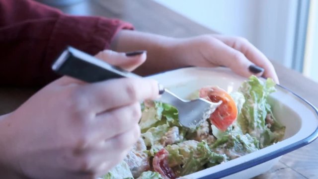 A lovely young woman eats Caesar salad mixed in an iron bowl. Street food, unhealthy junk food. Problems of obesity and healthy eating. Close-up. Slow motion.