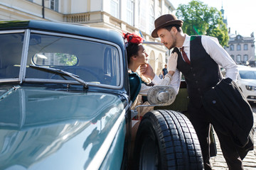 Woman dressed in old-fashioned style sits in a retro car together with her man