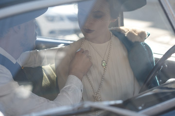 Woman dressed in old-fashioned style sits in a retro car together with her man