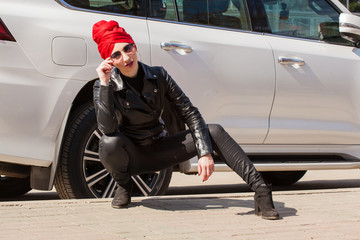 Stylish cheeky Muslim girl with a fashionably tied headscarf turban on her head in a red coat. Screaming image of a modern woman in the city against the backdrop of architecture