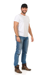 Smiling Handsome Man In Jeans, White T-shirt And Black Cap Is Standing And Looking At Camera